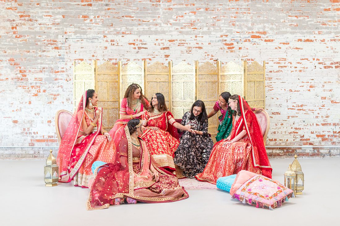 Indian wedding mehndi henna party with the bridesmaids and bride in pink and red saris. Photo created by Mikkel Paige Photography, planning by Harmony Weddings NC.