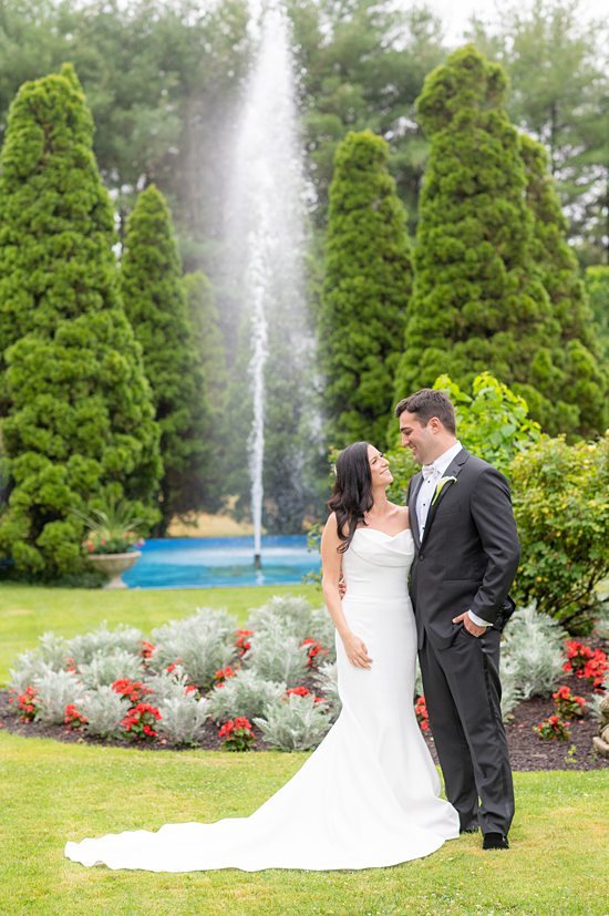 Rebecca and Dan, a bride and groom, at a wedding at The Carltun on Long Island, in the garden in front of a fountain.