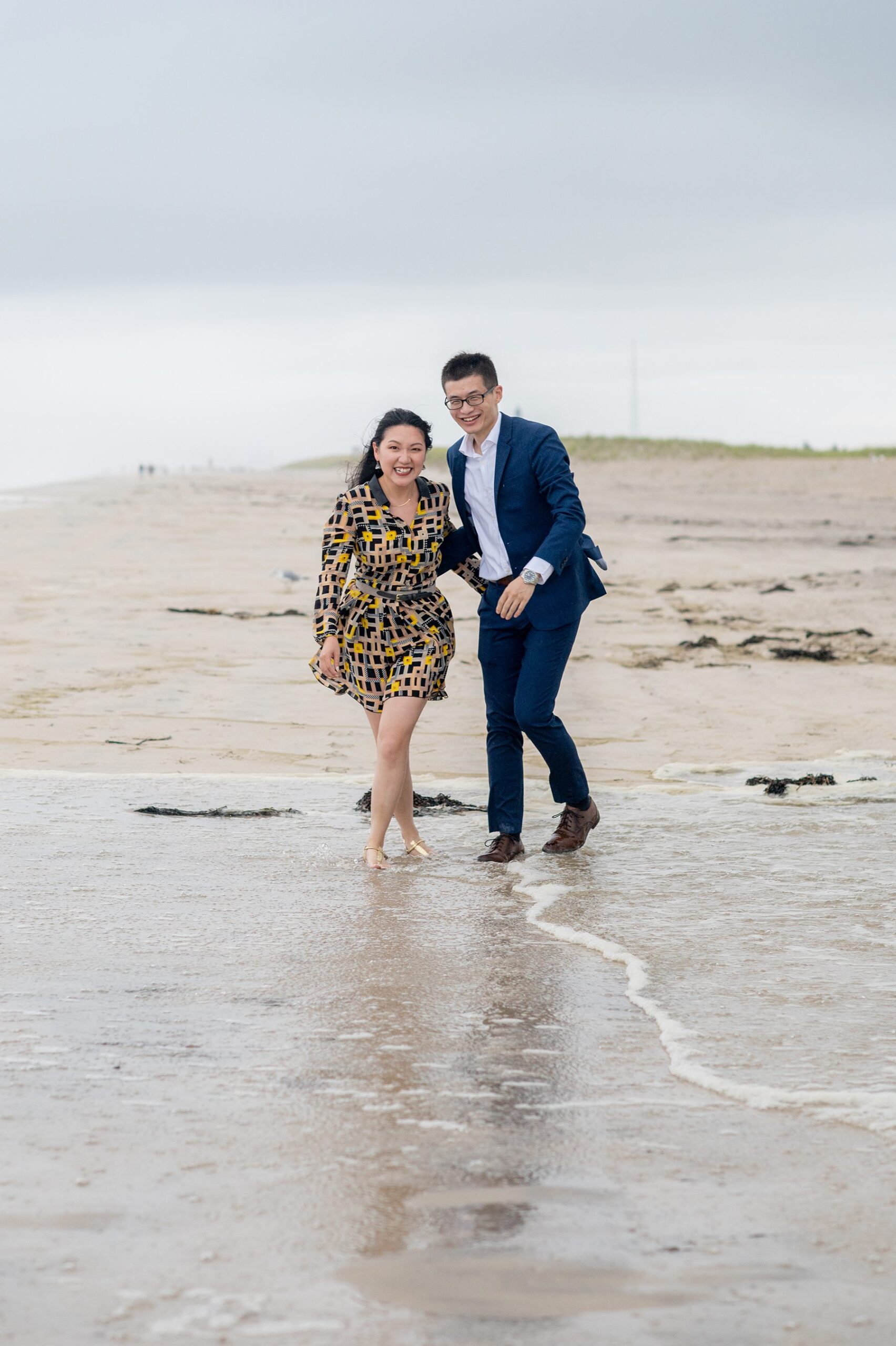 Photo of a couple in dress clothes with the ocean sand beneath them for a proposal on Robert Moses State Park Beach on Long Island.