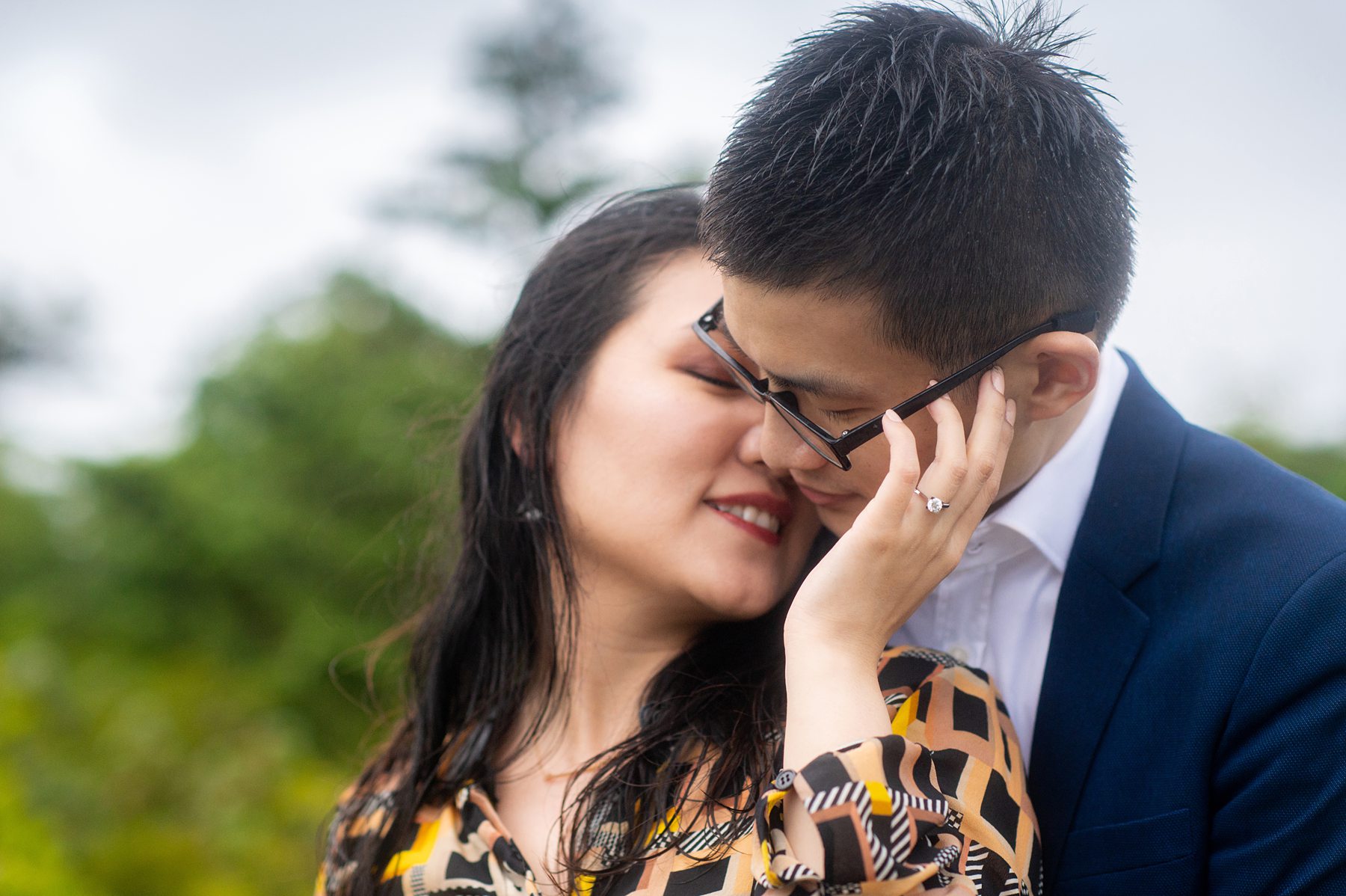 Photo of a couple at the beach with greenery blurred behind them on Long Island, and the woman's engagement ring in focus.