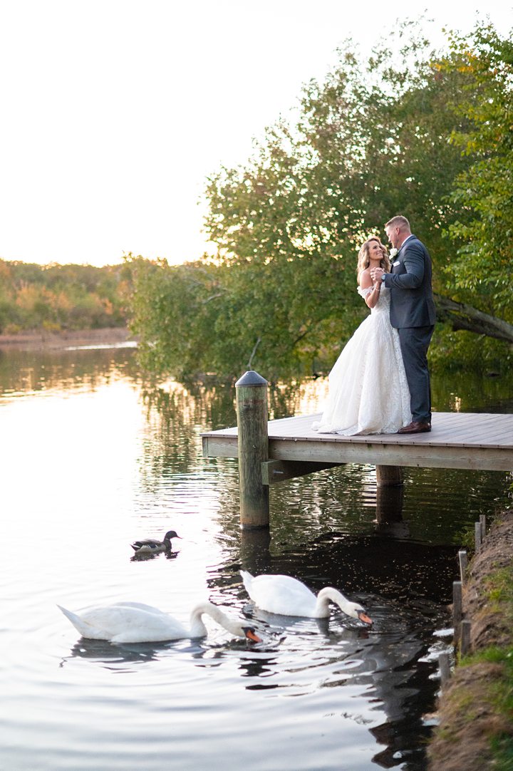 Bride and groom at their Mill at Spring Lake NJ wedding with swans in the lake. Image by Mikkel Paige Photography.