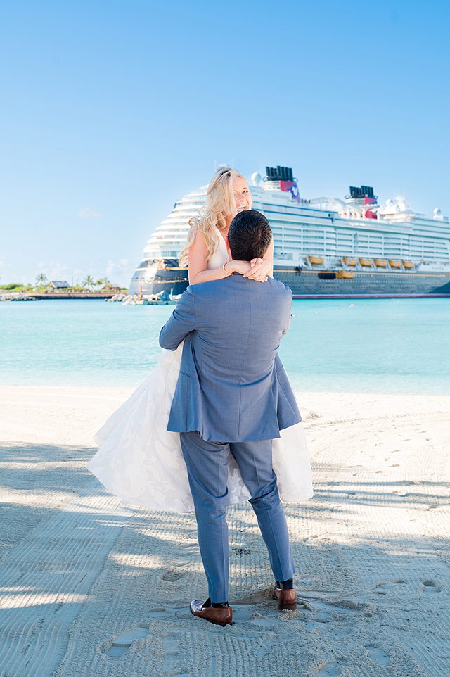 Bride and groom on the beach with Disney Wish in the background for Castaway Cay wedding photos the day after their Disney Cruise Line celebration, with pictures by Mikkel Paige Photography.