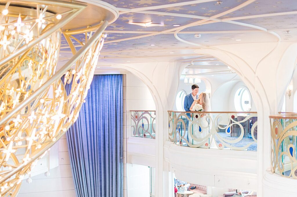 Disney Wish wedding photos by Mikkel Paige Photography of the bride and groom on a deck overlooking the Grand Hall chandelier.