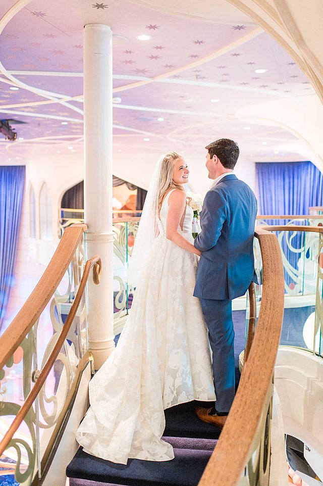 Disney Wish wedding photos by Mikkel Paige Photography of the bride and groom looking at each other on the Grand Hall stairs.