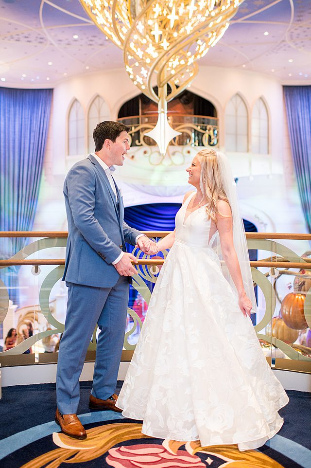 Disney Wish wedding photos by Mikkel Paige Photography of the bride and groom on a deck overlooking the Grand Hall chandelier.