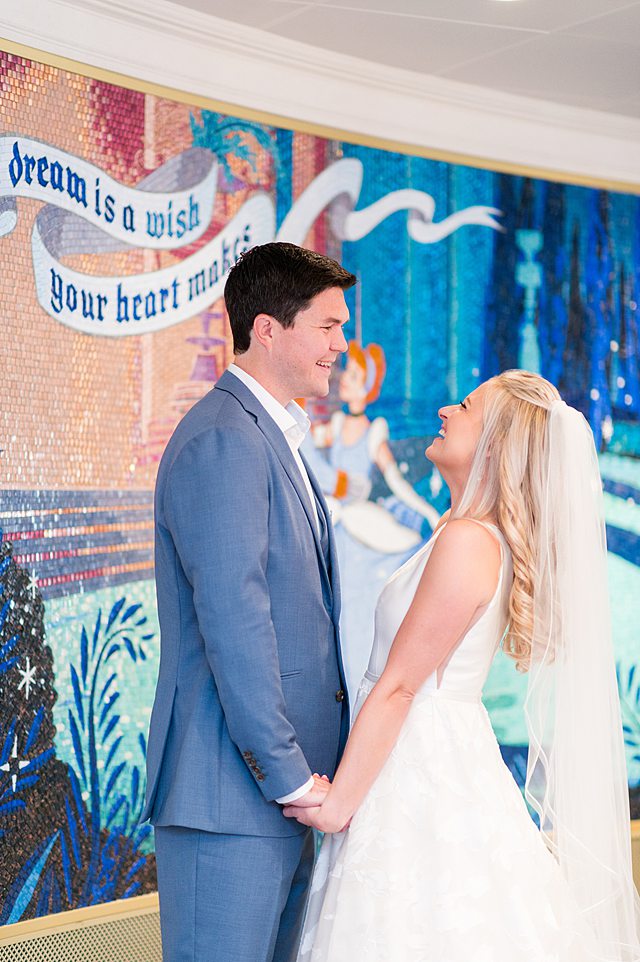 Bride and groom smiling at each other by a Cinderella mosaic in their Disney Wish wedding photos by Mikkel Paige Photography.