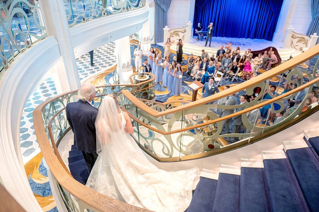 Bride and her father walking down the grand staircase on Disney Wish for a Grand Hall wedding. Photos by Mikkel Paige Photography.