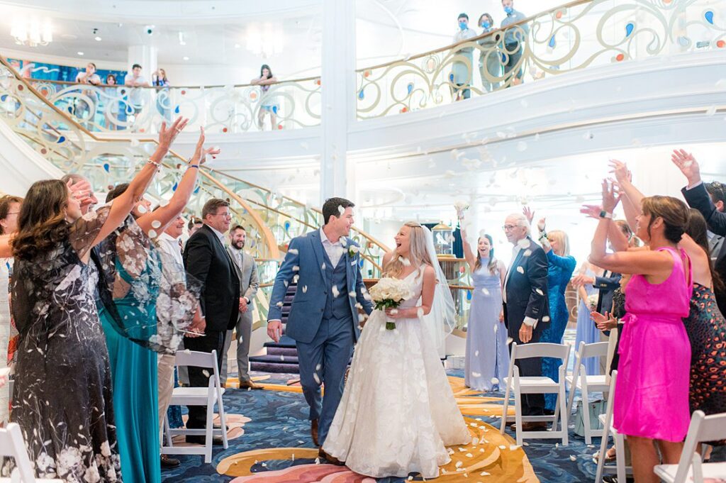 Couple smiling during a rose petal toss at their wedding ceremony in the grand hall on Disney Wish. Photos by Mikkel Paige Photography.