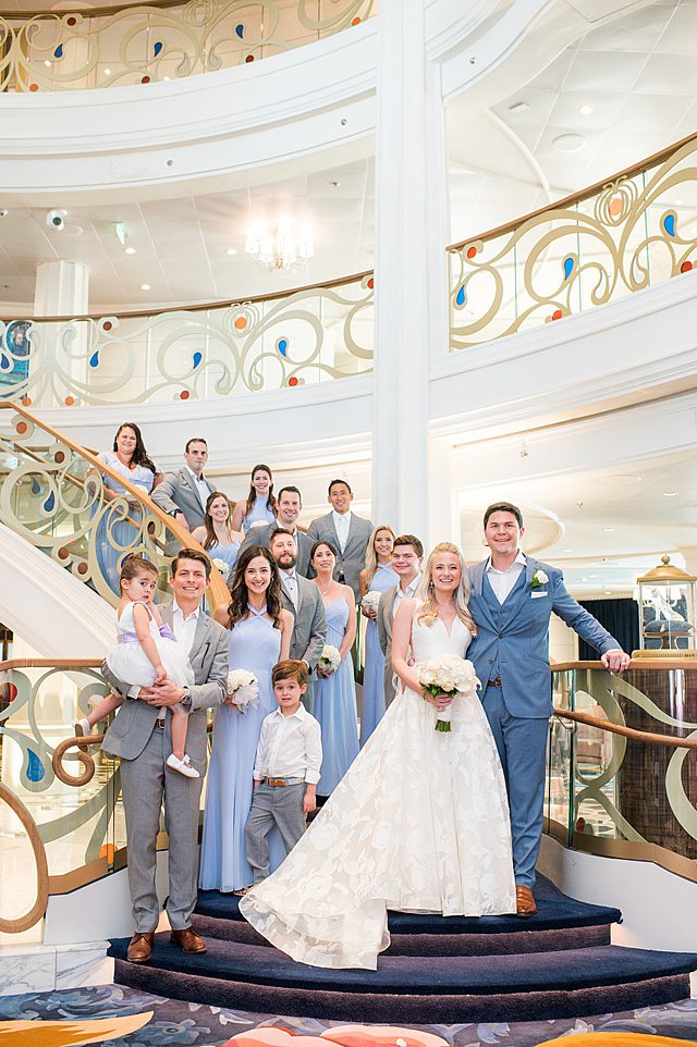 Wedding party picture with the bride, groom, bridesmaids and groomsmen on the grand hall staircase on Disney Wish. Photos by Mikkel Paige Photography.