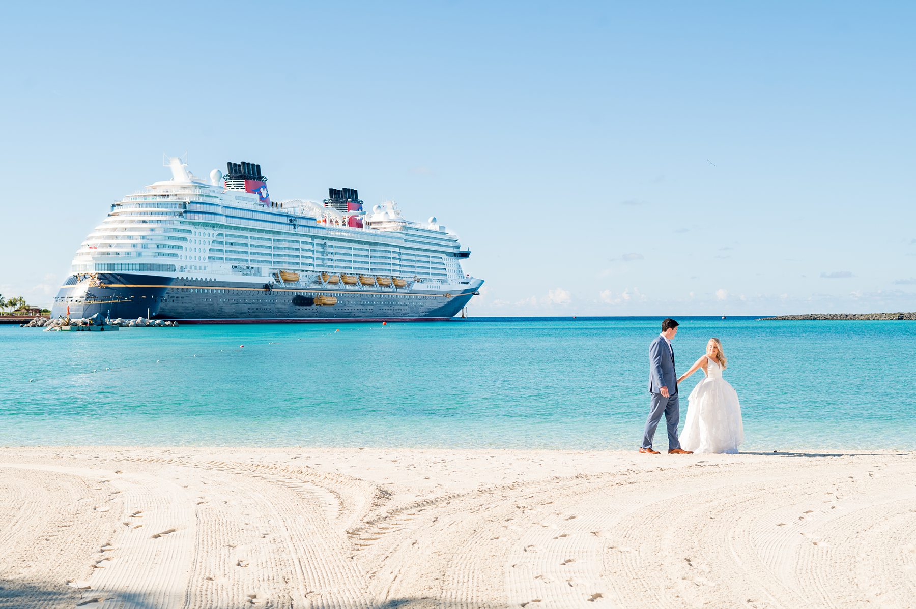 Couple on Castaway Cay beach with the Disney Wish cruise ship in the background. Image by Mikkel Paige Photography.