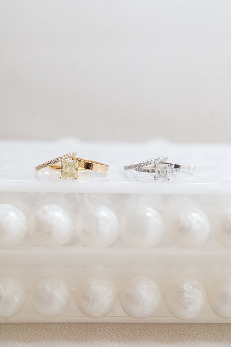 Two sets of wedding bands for two brides on a white pearl purse.