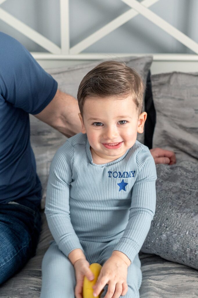Boy in blue smiling up on the camera from a bed.