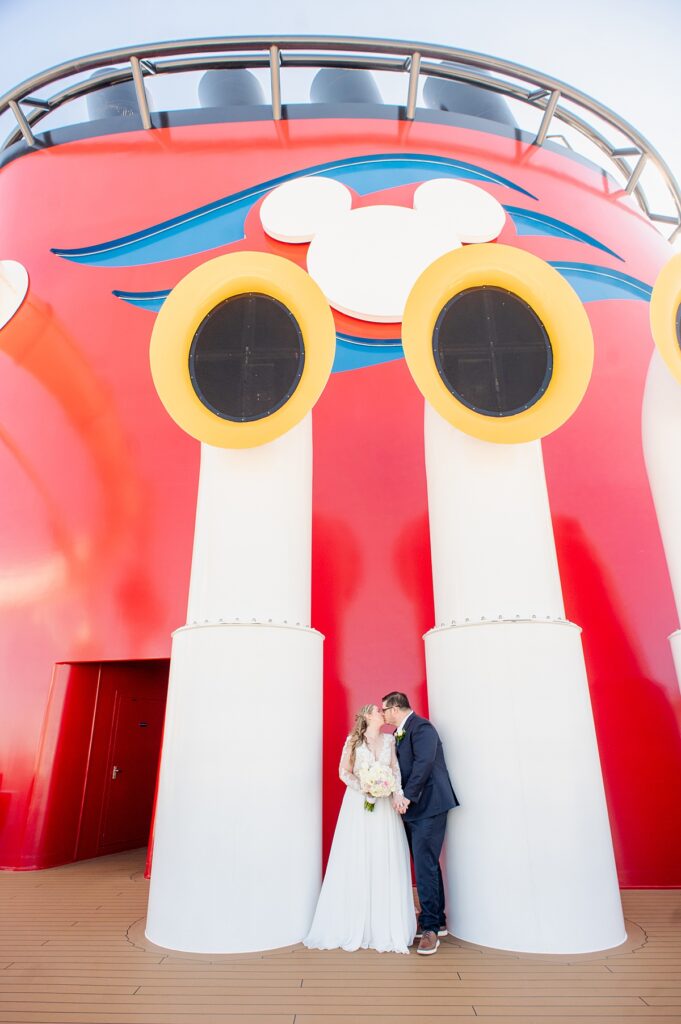 Bride and groom by the Disney Cruise Line stack in red, white, blue and yellow, on Disney Wish for their wedding.