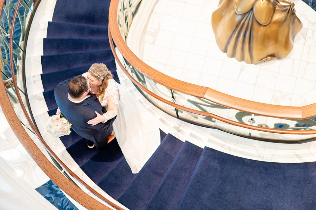 Bird's eye view looking down on the bride and groom on the staircase of the Grand Hall on Disney Wish for their wedding.