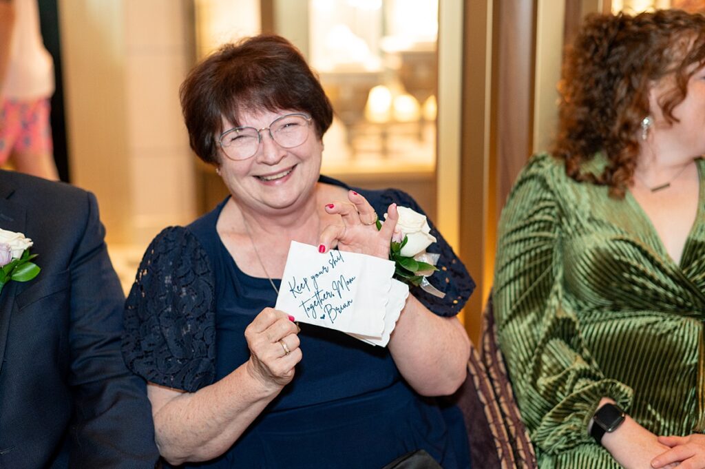 Mother of the groom holding an embroidered handkerchief and smiling.