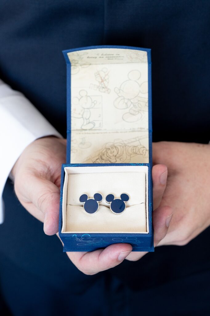 Hands holding a small box with blue Mickey Mouse shaped cufflinks for a Disney Wish Bayou wedding.